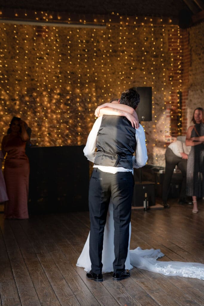Bride and groom hugging during their first dance under fairy lights in the barn