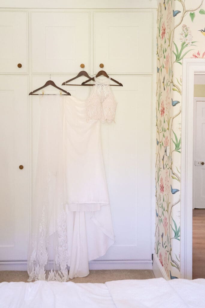 Wedding dress with a lace bodice hanging on a white wardrobe beside floral wallpaper at Cissbury House