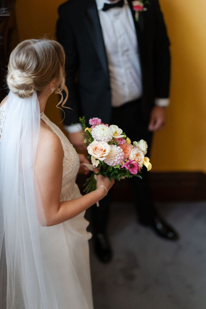 Bride holding her bouquet beside her brother at the foot of the stairs before the ceremony