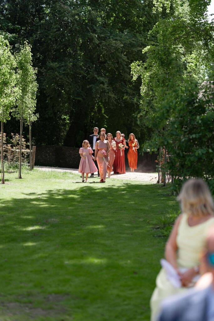 Bridesmaids in rust and pink dresses walking across the lawn to the outdoor ceremony
