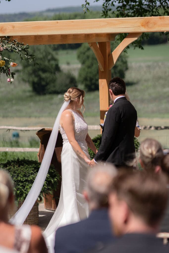 Bride and groom facing each other under the flower-covered pergola during their outdoor ceremony