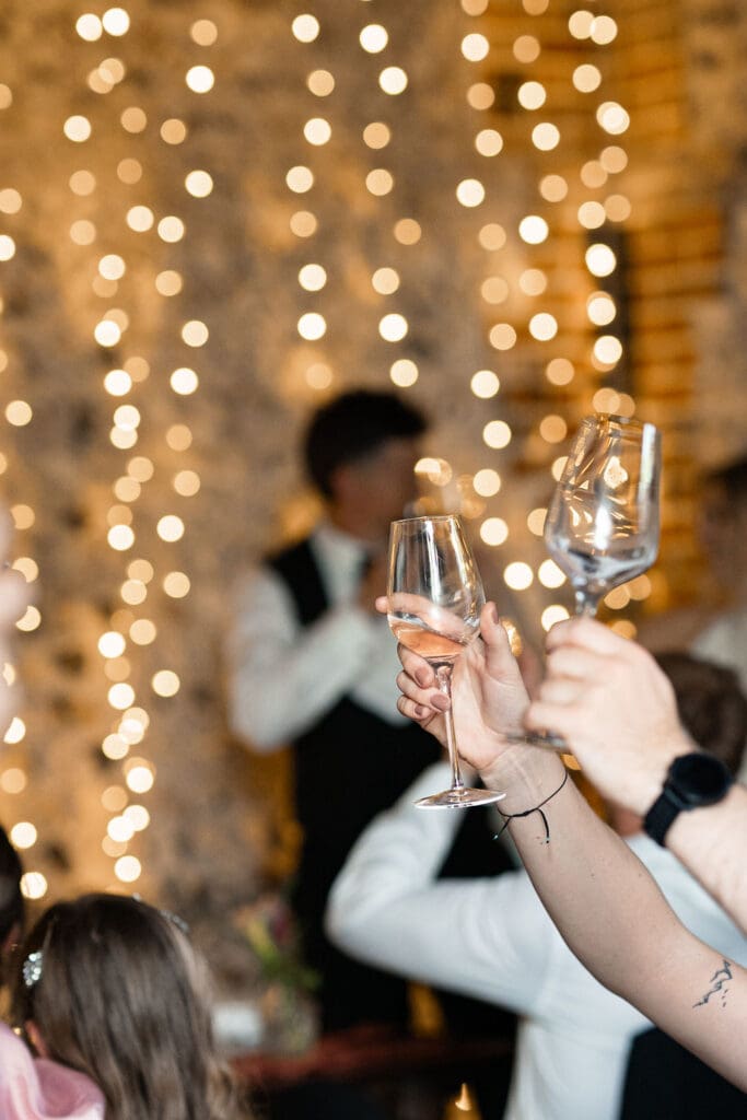 Guests raising their glasses for a toast in front of fairy lights in the barn