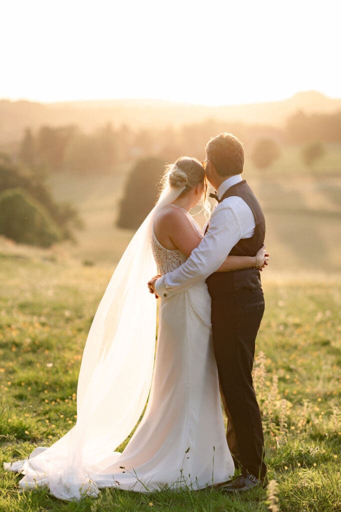 Bride and groom holding each other in the fields at sunset, taken by their Cissbury Barns wedding photographer