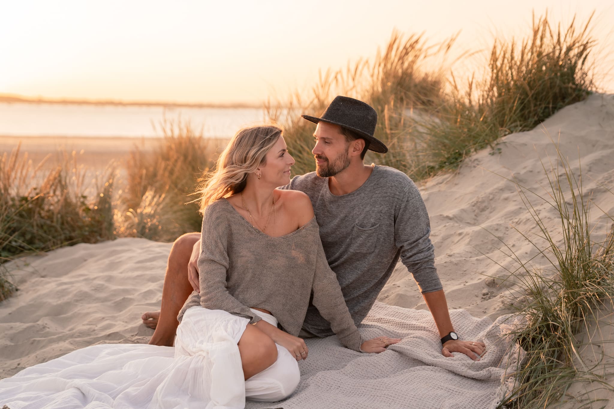 Couple sat on a blanket on the beach at sunset