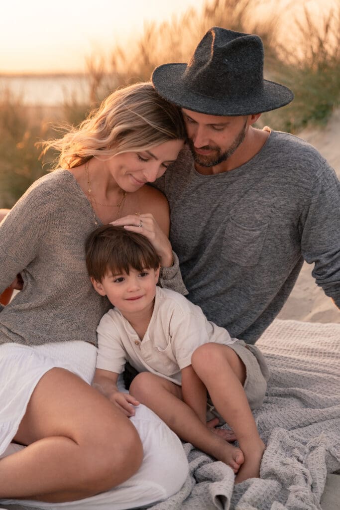 Family of three sat on West Witterings beach at sunset during family photoshoot